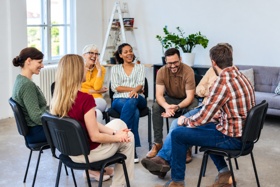 Group of adults smiling and talking in a circle during a support group session for people learning how to safely detox from alcohol